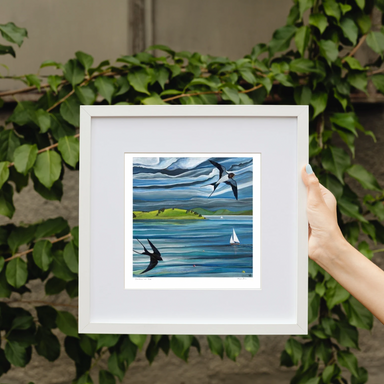 Framed primt of Swallows and Sails,  of birds over water with sailboats, held by a hand against a leafy background. Strangford Lough, Northern Ireland 