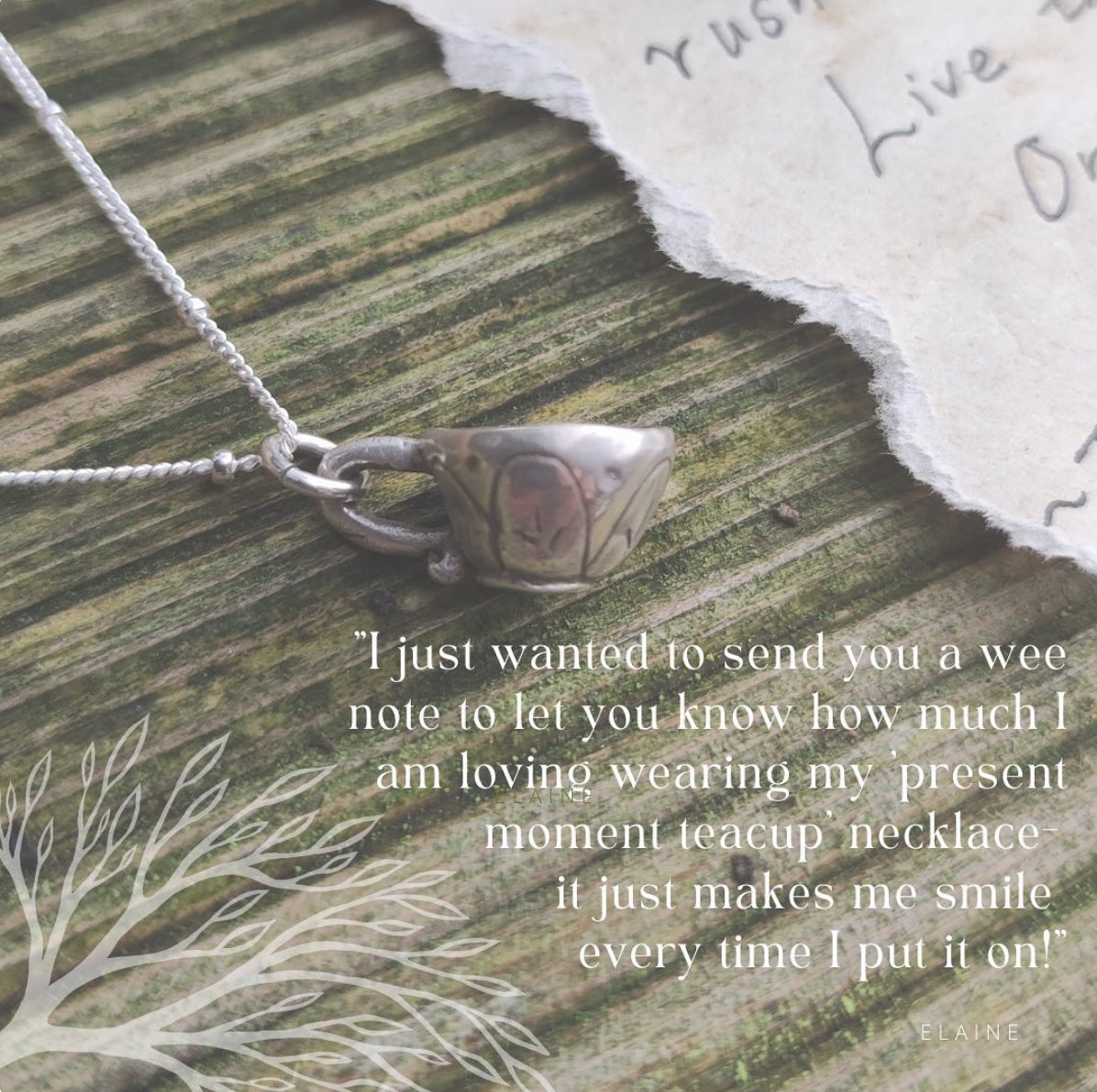 Teacup-shaped pendant on a necklace with a handwritten note on a wooden surface, testimonial from customer wild earth studio