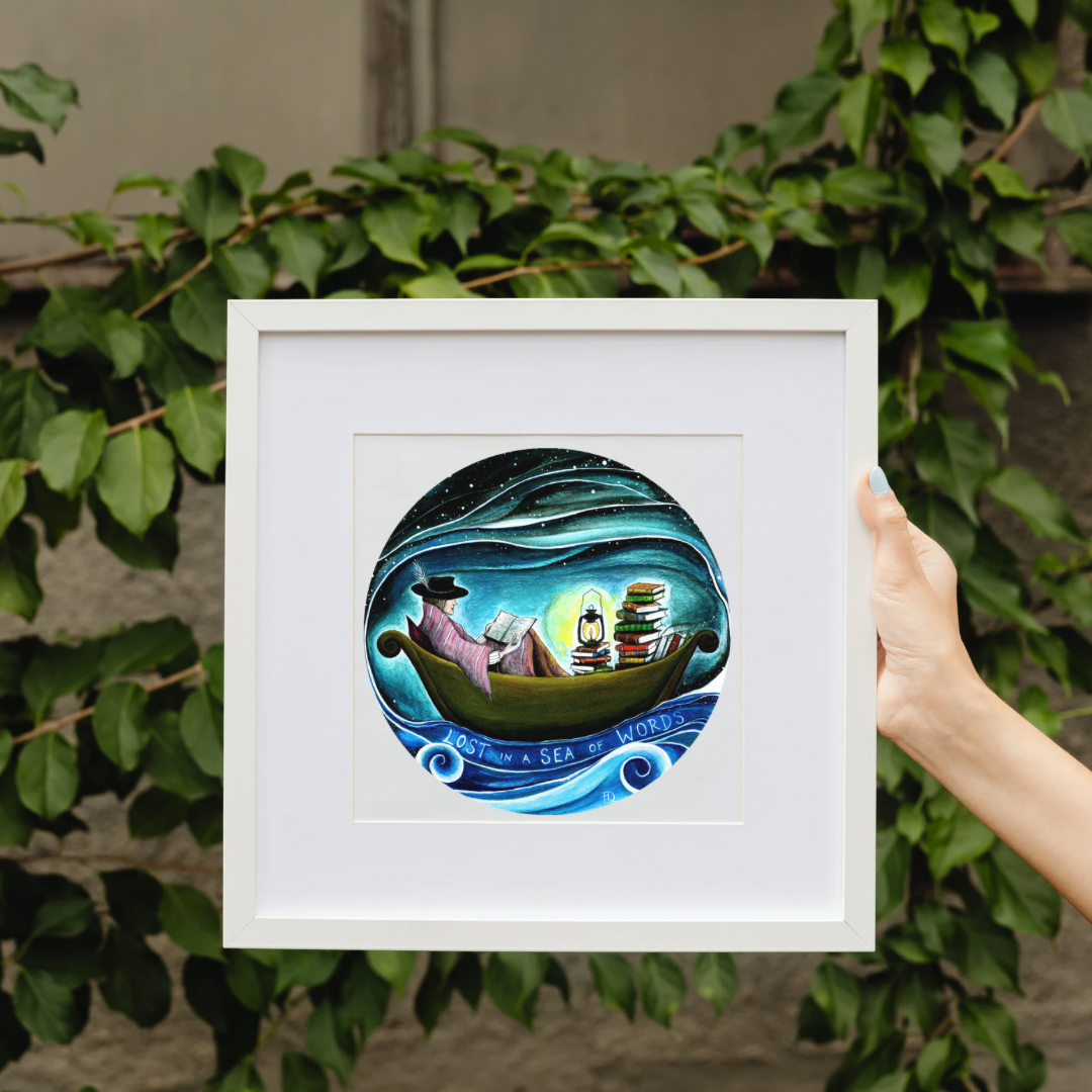 Framed artwork of a person on a boat with books at night, held by a hand against a leafy background. Lost in a Sea of Words, reading book art print, slow living art, gift for book lovers