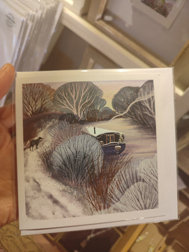 A square greeting card with an artistic winter scene depicted on it, held in a hand. The card has a blank inside for a personal message. Winter dog walk card, canal boat living art